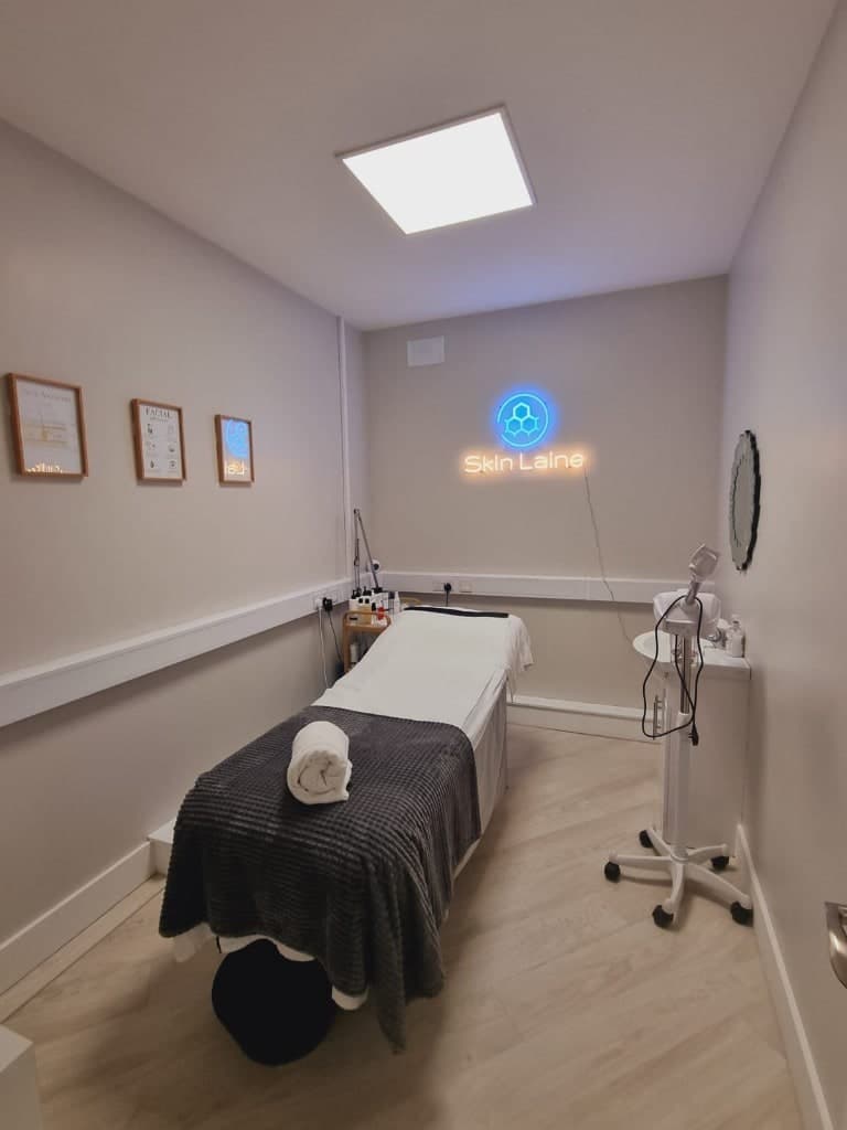 Treatment room at Skin Laine in Ballina with a prepared bed and glowing Skin Laine neon sign on the wall.